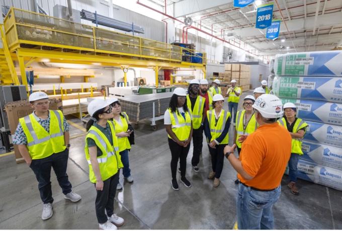 group of people in an industrial building wearing safety vests and white hard hats